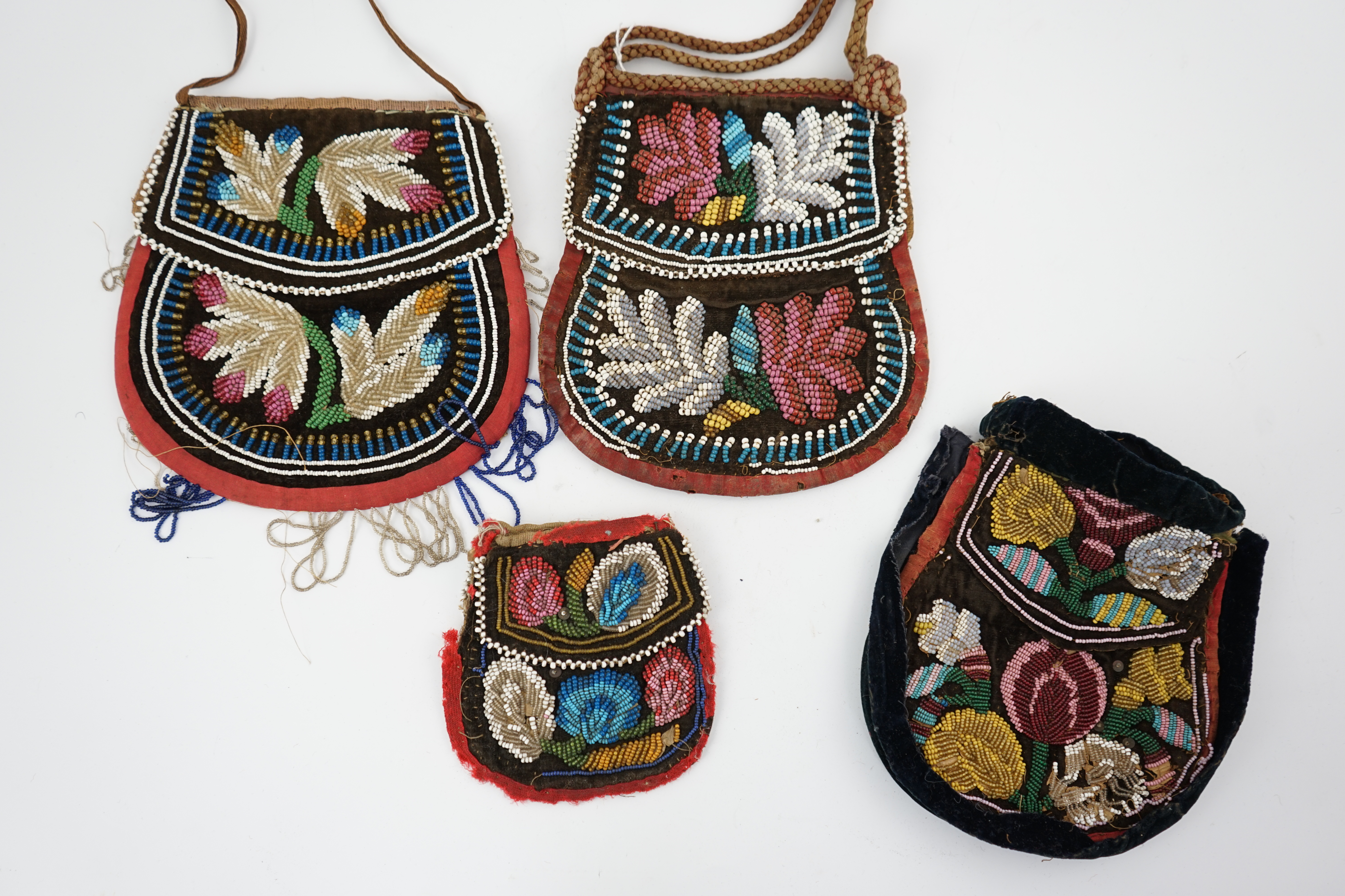 Four 19th century Iroquois Native American beaded bags, three large and one smaller, all bags worked in various colours and differing designs, all with flaps and same pattern both sides, largest 19cm high. Condition - al